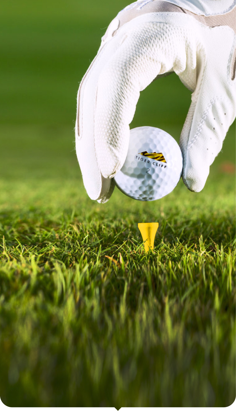 Golf ball on a tee with a gloved hand about to hit it on a green background