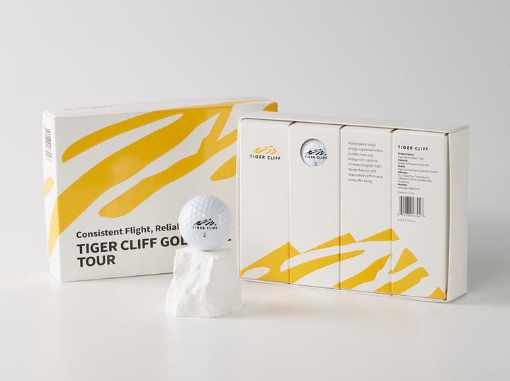 Tiger Cliff Tour golf ball on a rock, next to its box with yellow stripes.