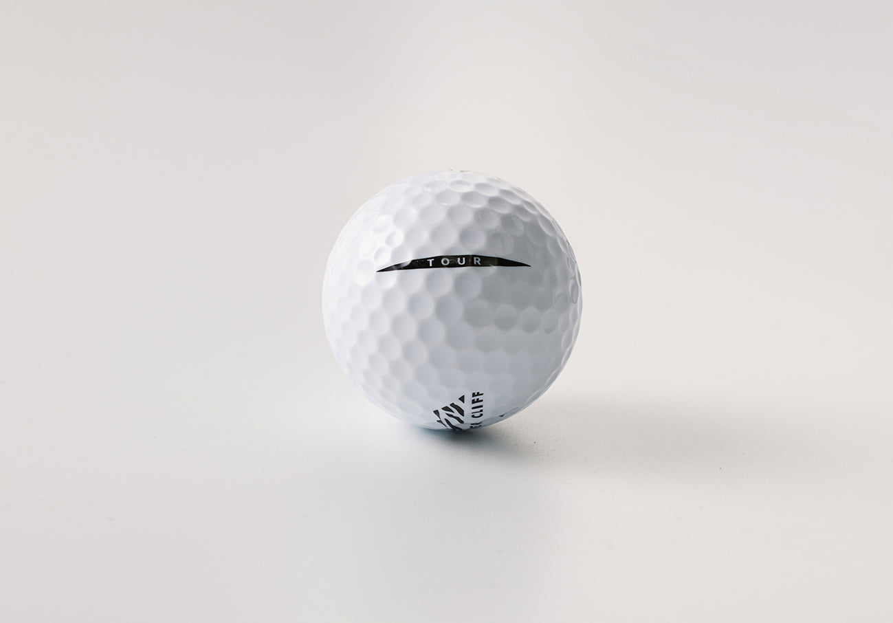 Close-up of a textured white golf ball with "TOUR" and "Cliff" printed on it.